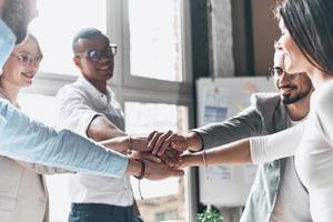 To success Young modern people in smart casual wear holding hands on top of one another in a symbol of unity while working in the creative office photo