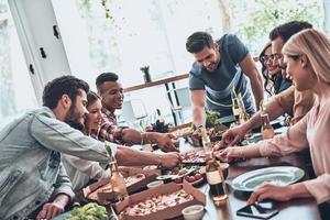 Choosing the best slice. Group of young people in casual wear eating and smiling while having a dinner party photo