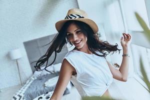 Spending carefree time. Attractive young woman looking away and smiling while standing in the bedroom at home photo