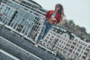 Perfect style. Full length of beautiful young woman in casual wear looking away while running down the stairs outdoors photo