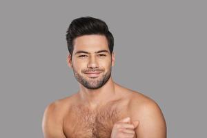 feliz y guapo. un joven apuesto mirando a la cámara y sonriendo mientras se enfrenta a un fondo gris foto