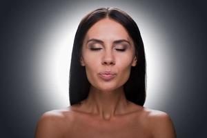 Kiss for you. Portrait of beautiful young shirtless woman keeping eyes closed and grimacing while standing against grey background photo