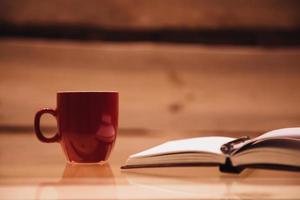 Coffee break. Close-up of coffee cup and notebook on glass table with wooden background photo