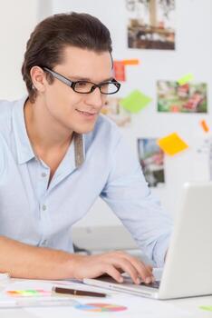Creative worker. Cheerful young man in glasses working on computer and smiling while sitting at his working place photo