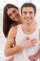 Waking up together. Beautiful young loving couple sitting together in bed and smiling photo