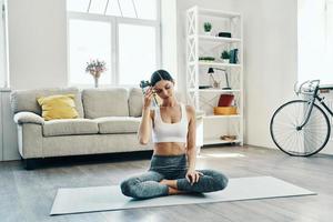 Just a minute to rest. Beautiful young woman in sports clothing practicing yoga and drinking yoga while spending time at home photo