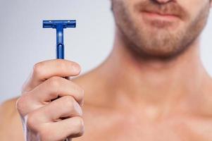 This razor irritates my skin. Cropped image of handsome young man shaving and grimacing while standing isolated on grey background photo