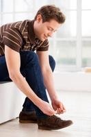 Tying shoelaces. Side view of handsome young man tying shoelaces and smiling photo