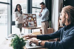 Giving business advice. Group of young business people using blackboard with adhesive notes while working in the office photo