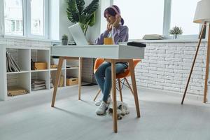 Confident young woman in headphones using laptop while sitting at her working place photo