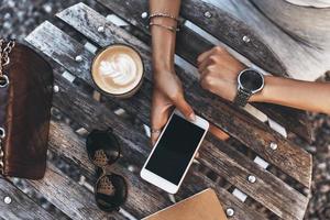 Modern female. Close-up top view of young woman holding a smart phone while sitting in restaurant outdoors photo