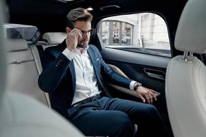 Confident manager. Handsome young man in full suit adjusting his eyewear while sitting in the car photo