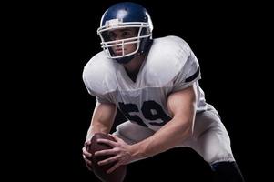 Getting ready to fight for this game.  American football player holding ball and looking away while standing against black background photo