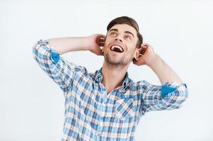 Incredible news. Surprised young man in shirt smiling and looking up while standing against white background photo