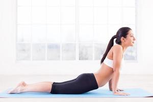 Working out. Side view of beautiful young Indian woman training on yoga mat photo