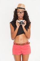 Funky photographer. Surprised young African woman in glasses and funky wear holding camera and keeping mouth open while standing against white background photo