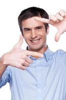 Businessman focusing at you. Portrait of handsome young man in blue shirt looking at camera and focusing at you with fingers while standing isolated on white photo