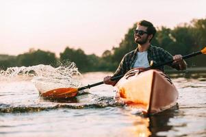 Enjoying life on river. Handsome young smiling man splashing water while kayaking on river photo