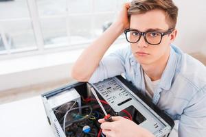 cansado de trabajar. vista superior de un joven apuesto que sostiene un destornillador para reparar la computadora y se ve cansado mientras está sentado en su lugar de trabajo foto