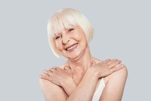 Fresh and clean. Beautiful senior woman looking at camera and smiling while standing against grey background photo