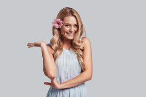 Something in the way she looks... Attractive young woman with a flower in hair looking at camera and smiling while standing against grey background photo