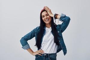 Attractive young woman in bandana looking at camera and smiling while standing against grey background photo