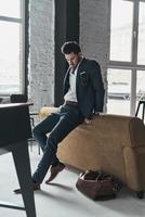 Taking some time to think. Full length of thoughtful young man in full suit looking away while leaning on the sofa photo