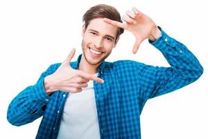 Finger frame. Handsome young man gesturing a finger frame and looking at camera while standing against white background photo