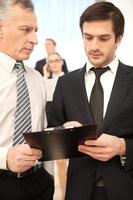 Working moments. Two business men discussing something while moving by staircase with people on background photo