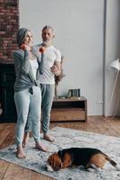 Full length of senior couple in sports clothing exercising using hand weight and smiling while spending time at home photo