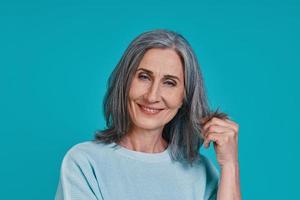 Headshot of mature beautiful woman looking at camera and smiling while standing against blue background photo