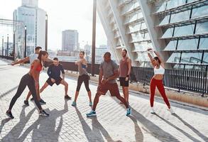 Longitud total de personas con ropa deportiva calentándose y estirándose mientras hacen ejercicio al aire libre foto
