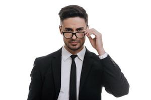 Confident manager. Handsome young man in full suit adjusting his eyeglasses and looking at camera while standing against white background photo