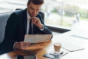 Handsome young businessman in full suit reading menu while sitting in the restaurant photo