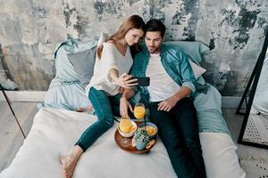 Let me take a selfie Top view of beautiful young couple taking selfie and smiling while spending time in bed at home photo