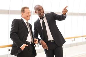 Business people. Two cheerful business men standing close to each other while one of them pointing away and smiling photo