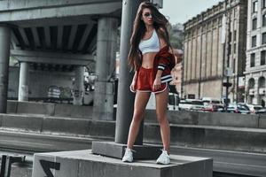 Feeling free and confident. Full length of attractive young woman in sport clothing looking away while posing under the bridge outdoors photo