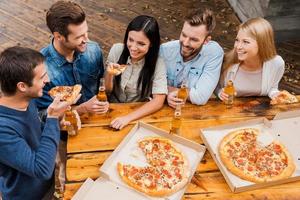 Carefree time with friends. Top view of five cheerful peopleholding bottles with beer and eating pizza while standing outdoors photo