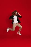 Full length of happy young man in casual clothing smiling and gesturing while hovering against red background photo