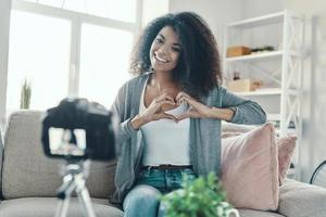 Cute young African woman showing heart with her hands and smiling while making social media video photo