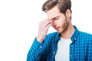 Feeling exhausted. Frustrated young man massaging his nose and keeping eyes closed while standing against white background photo