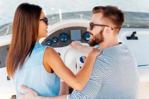 Their love is bigger than ocean. Happy young couple looking at each other and smiling while driving yacht photo