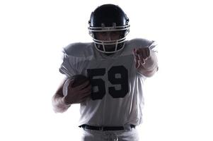 Choosing you.  American football player holding ball and pointing at camera while standing against white background photo