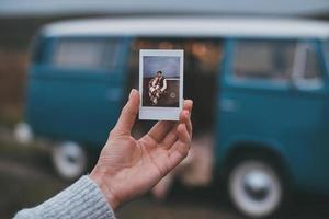 gratos recuerdos. primer plano de una mujer joven sosteniendo una foto de una pareja joven mientras está de pie al aire libre cerca de la mini furgoneta de estilo retro azul