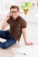 Surfing web at home. Top view of handsome young man in glasses working on laptop while sitting on the floor at his apartment photo
