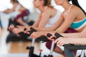 Exercising on gym bikes. Cropped image of tree young women in sports clothing exercising on gym bicycles