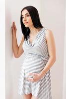 Expecting a baby. Thoughtful pregnant woman leaning at the wall and looking away photo