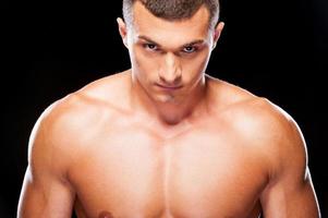 Power inside him. Portrait of serious young shirtless man looking at camera while standing against black background photo