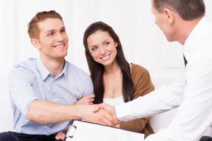 Sealing a deal. Happy young man shaking hand to financial agent while sitting together with his wife photo