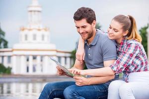 Choosing the place to go next. Happy young tourist couple sitting near beautiful building and examining map together photo